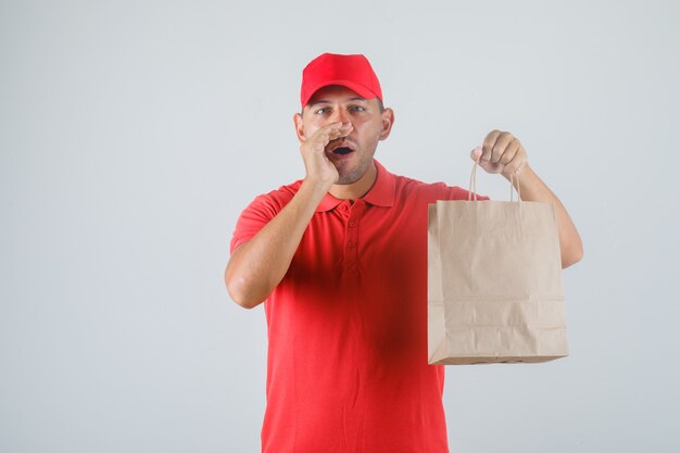 Repartidor sosteniendo una bolsa de papel y gesticulando en vista frontal uniforme rojo.