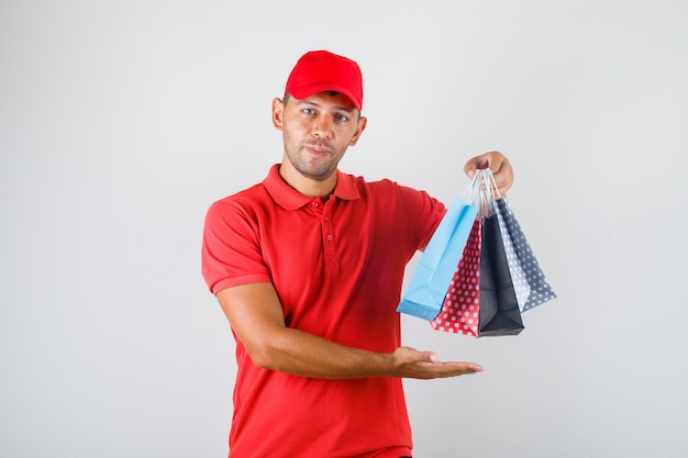 Repartidor sosteniendo bolsas de papel de colores en uniforme rojo
