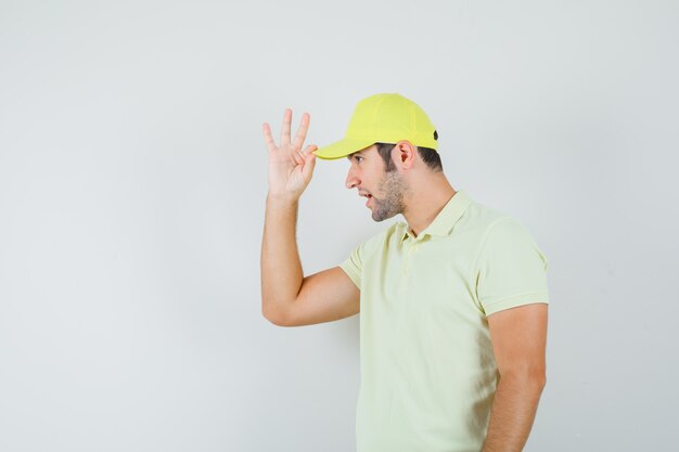 Repartidor sosteniendo su gorra en uniforme amarillo y luciendo guapo. vista frontal.