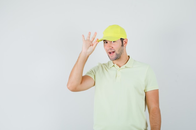 Repartidor sosteniendo su gorra en uniforme amarillo y mirando elegante, vista frontal.