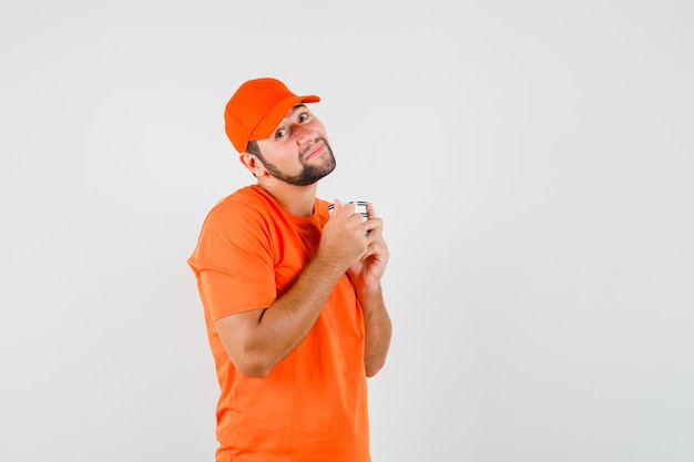 Repartidor sosteniendo una taza de bebida en camiseta naranja, gorra y aspecto lindo. vista frontal.