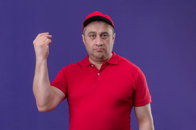 Foto gratuita repartidor con uniforme rojo y gorra disgustado con la mano levantada sobre la pared púrpura aislada