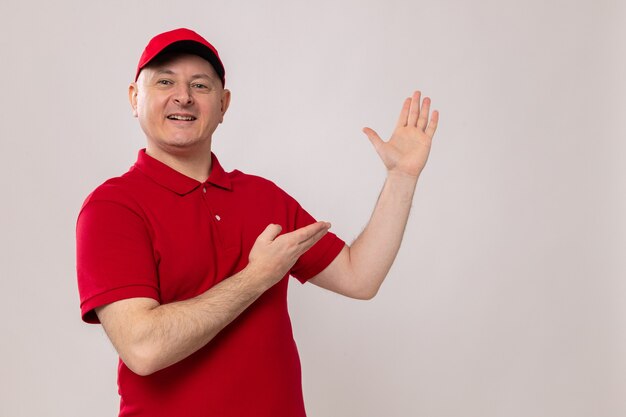 Repartidor en uniforme rojo y gorra mirando sonriendo confiado presentando con los brazos de sus manos