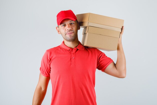 Repartidor en uniforme rojo sosteniendo cajas de cartón sobre su hombro