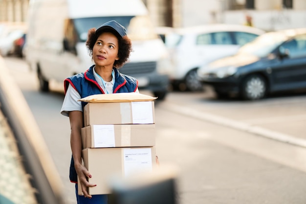 Una repartidora afroamericana cargando paquetes mientras camina por la calle y busca la dirección