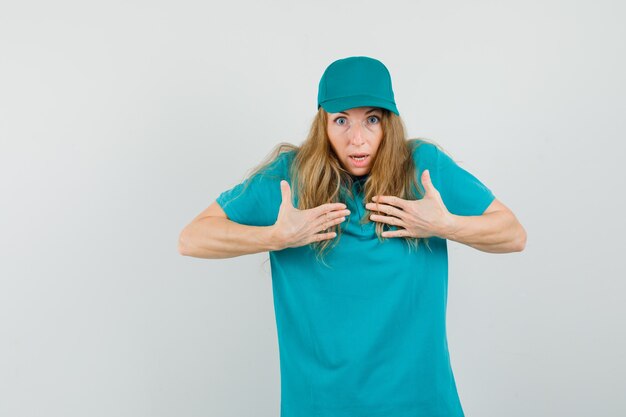 Repartidora en camiseta, gorra apuntando a sí misma para preguntarme y luciendo agitada