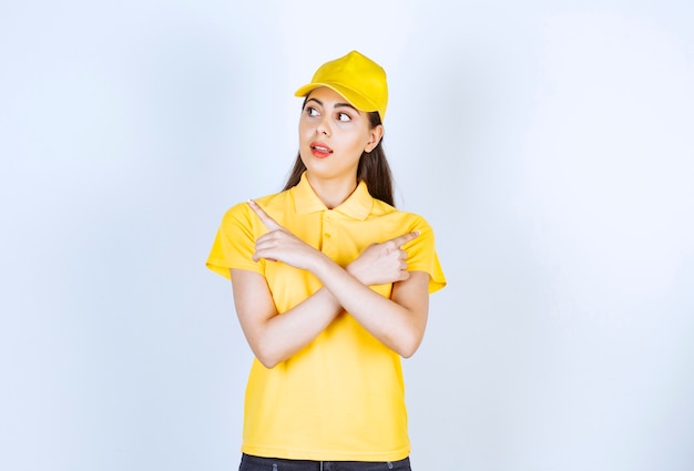 Repartidora joven en camiseta amarilla y gorra apuntando a algún lugar en blanco.