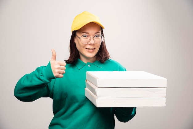 Repartidora mostrando un pulgar hacia arriba y sosteniendo cartones de pizza sobre un fondo blanco. Foto de alta calidad