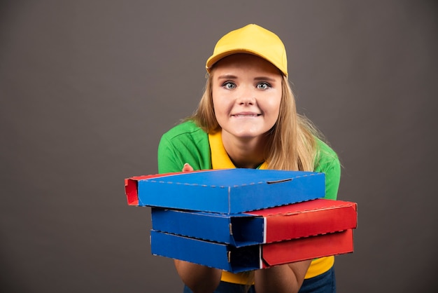 Repartidora sonriente en uniforme sosteniendo cartones de pizza.