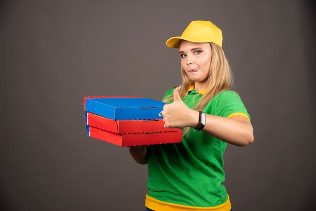 Repartidora sosteniendo cartones de pizza y mostrando el pulgar hacia arriba.