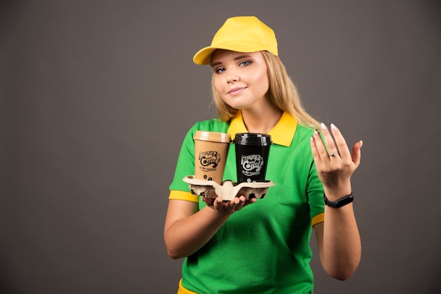 Repartidora sosteniendo tazas de café en la pared negra.