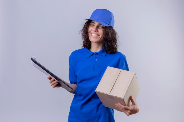 Repartidora en uniforme azul y gorra con paquete de caja y portapapeles sonriendo alegremente de pie en blanco