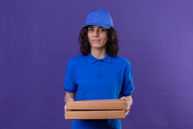 Repartidora en uniforme azul y gorra sosteniendo cajas de pizza sonriendo confiados de pie sobre el espacio púrpura