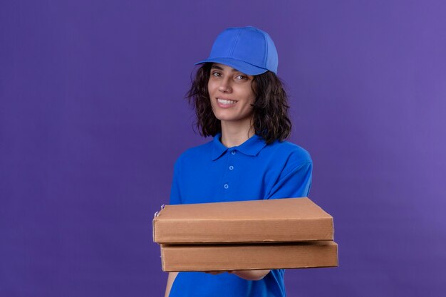 Repartidora en uniforme azul sosteniendo cajas de pizza positivo y feliz sonriendo amable permanente