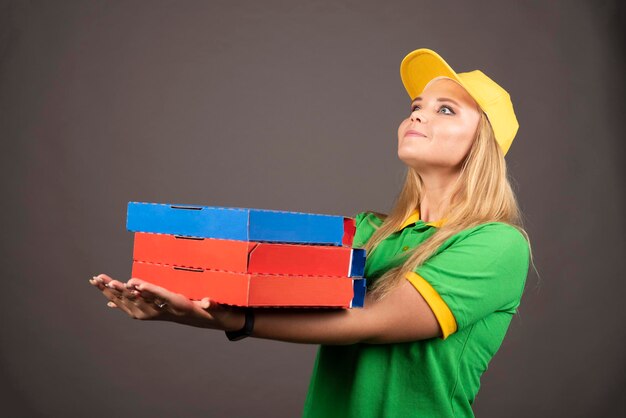 Repartidora en uniforme sosteniendo cartones de pizza. Foto de alta calidad