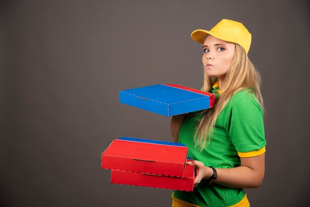 Repartidora en uniforme sosteniendo cartones de pizza.