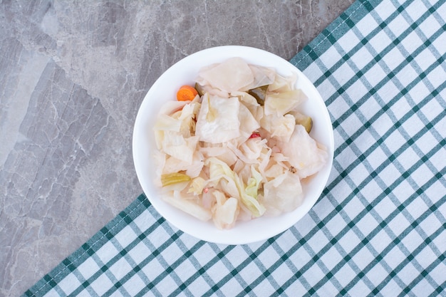 Repollo blanco en escabeche en un tazón blanco con mantel.