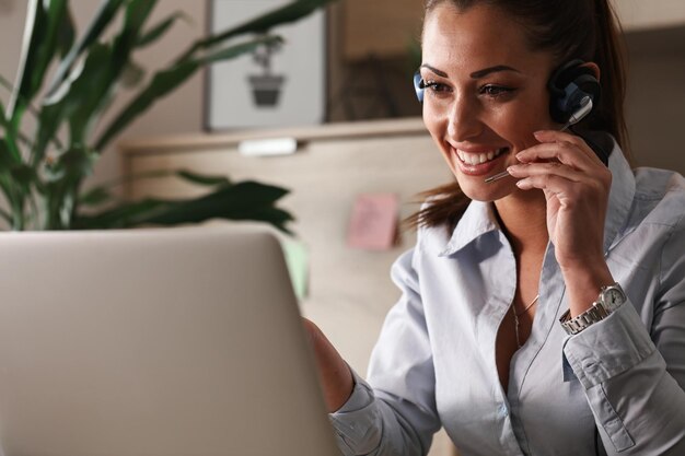 Representante de servicio al cliente feliz hablando con un cliente mientras usa una computadora portátil en la oficina
