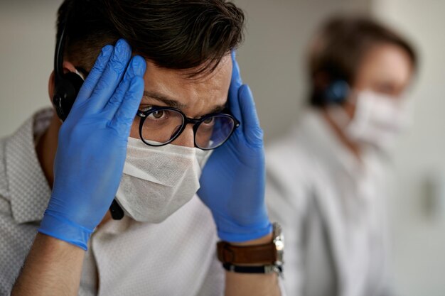 El representante del servicio de atención al cliente se siente cansado y le duele la cabeza mientras trabaja en el centro de llamadas durante la epidemia de coronavirus