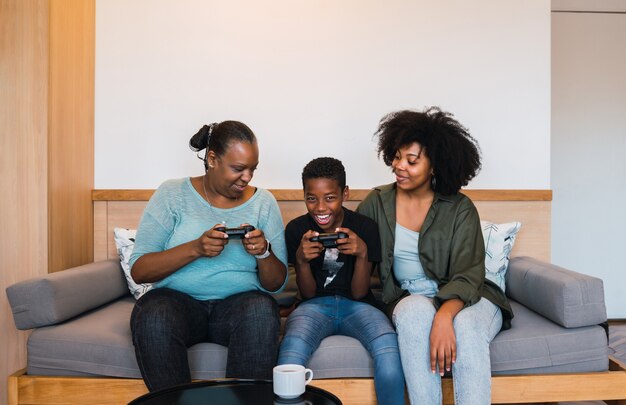 Retrato de abuela afroamericana, madre e hijo jugando videojuegos juntos en casa