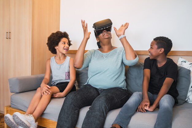 Retrato de abuela afroamericana y nietos jugando junto con gafas VR en casa. Concepto de familia y tecnología.