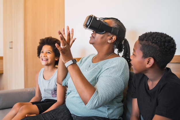 Retrato de abuela afroamericana y nietos jugando junto con gafas VR en casa