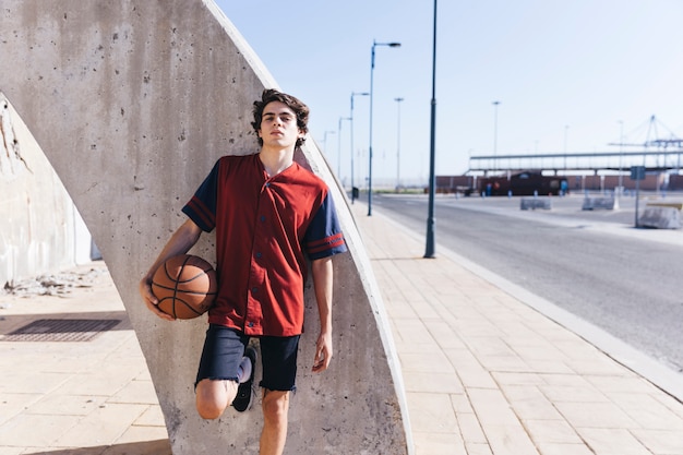 Retrato de un adolescente apoyado en la pared con baloncesto