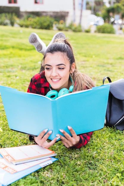 Foto gratuita retrato de una adolescente feliz tumbada en el césped leyendo el libro