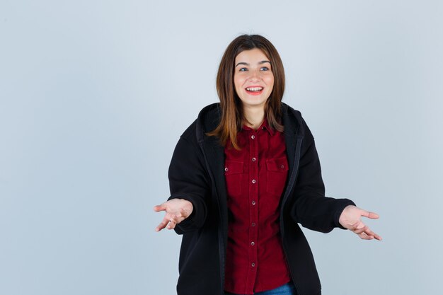 Retrato de una adolescente haciendo gesto de pregunta en camisa, abrigo y mirando alegre vista frontal