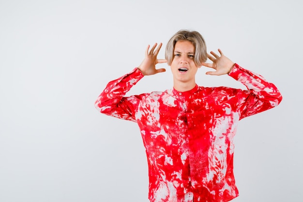 Retrato de adolescente varón rubio mostrando gesto de rendición en camisa de gran tamaño y mirando preocupado vista frontal