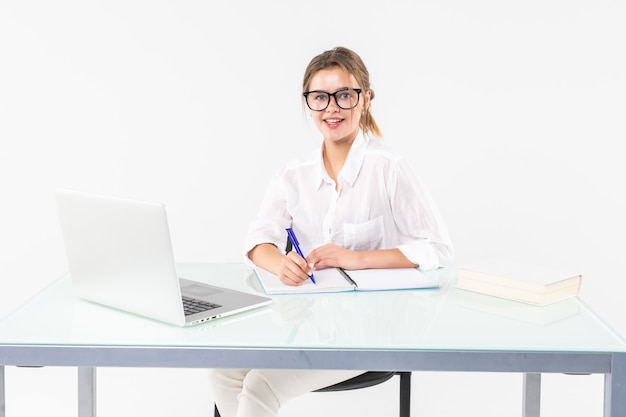 Retrato de una adorable mujer de negocios trabajando en su escritorio con una computadora portátil y documentos aislados sobre fondo blanco.