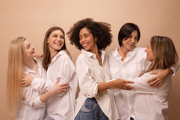 Retrato de adultos multiétnicos y mujeres jóvenes en camisas blancas abrazándose unos a otros sobre fondo marrón