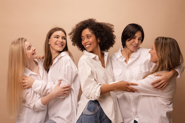 Retrato de adultos multiétnicos y mujeres jóvenes en camisas blancas abrazándose unos a otros sobre fondo marrón