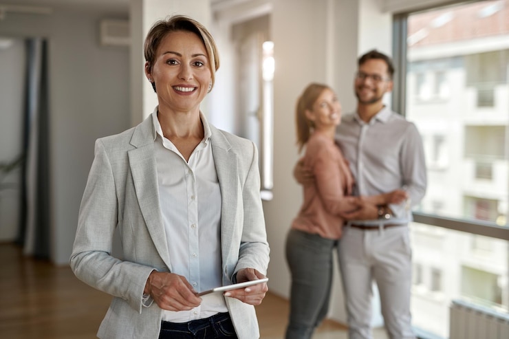 Foto gratuito retrato de una agente inmobiliaria mirando a la cámara mientras una pareja feliz está de pie en el fondo