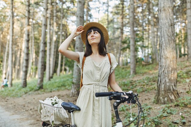 Retrato al aire libre de la atractiva joven morena con un sombrero en una bicicleta.