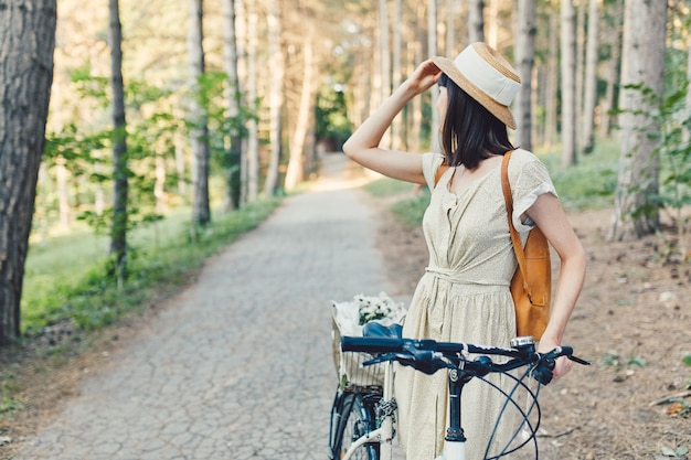 Retrato al aire libre de la atractiva joven morena con un sombrero en una bicicleta.