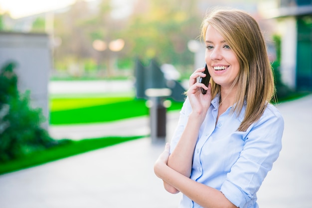 Retrato al aire libre de una hermosa mujer morena feliz o empresaria en sus años treinta hablando por su teléfono celular