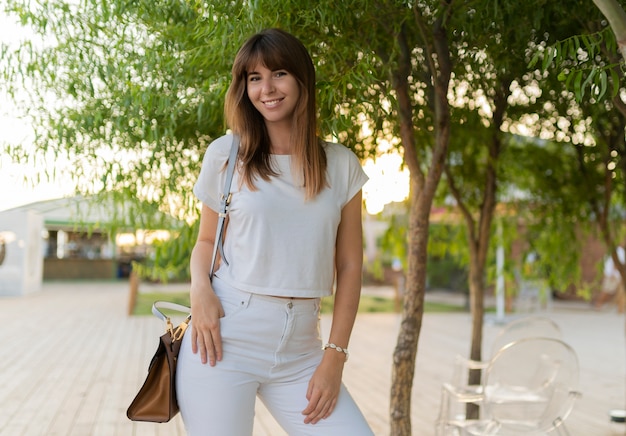 Retrato al aire libre de mujer alegre en camiseta blanca y jeans caminando en el parque.