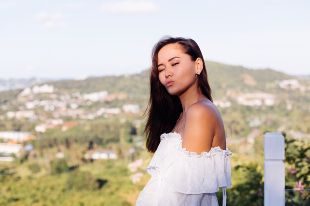 Retrato al aire libre de mujer asiática en vestido blanco con collar y aretes