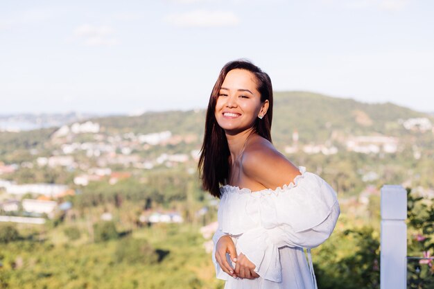 Retrato al aire libre de mujer asiática en vestido blanco con collar y aretes