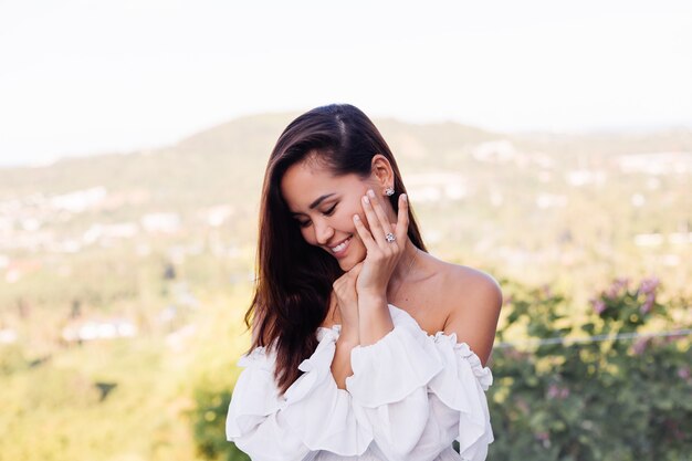 Retrato al aire libre de mujer asiática en vestido blanco con collar y aretes