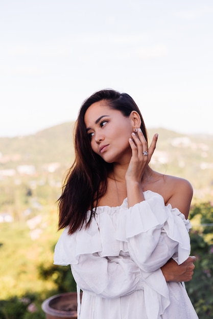 Retrato al aire libre de mujer asiática en vestido blanco con collar y aretes