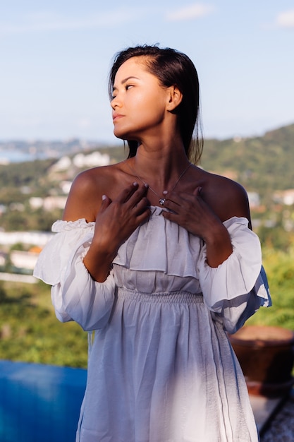 Retrato al aire libre de mujer asiática en vestido blanco con collar.