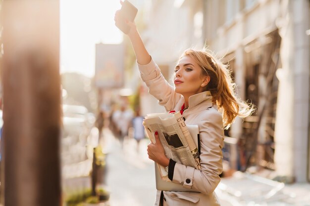 Retrato al aire libre de mujer de negocios activa en traje de moda esperando un taxi en la mañana