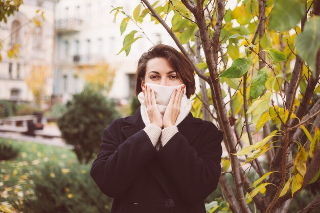 Retrato al aire libre de mujer en el parque vistiendo abrigo negro de invierno y pañuelo blanco