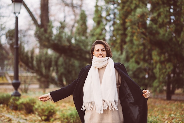 Retrato al aire libre de mujer en el parque vistiendo abrigo negro de invierno y pañuelo blanco