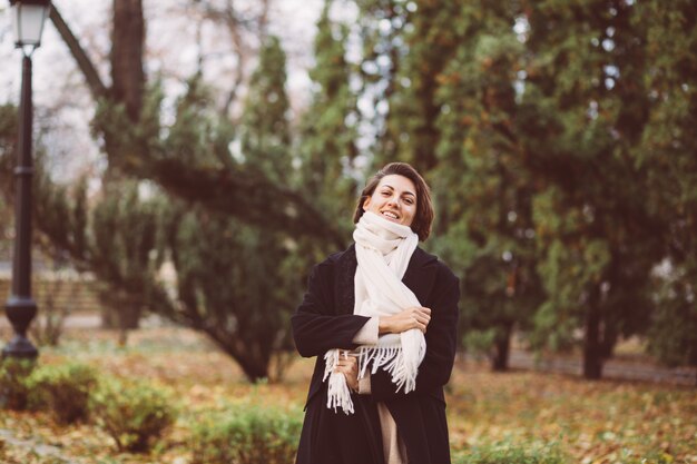 Retrato al aire libre de mujer en el parque vistiendo abrigo negro de invierno y pañuelo blanco