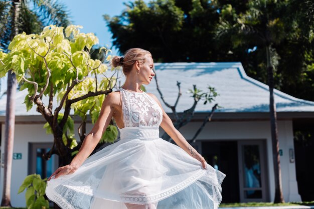 Retrato al aire libre de mujer en vestido de novia blanco en villa en día soleado, vista tropical