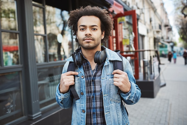 Retrato al aire libre de viajero elegante de piel oscura con peinado afro caminando en la calle.