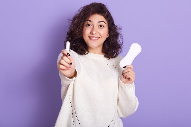 Retrato de alegre atractiva jovencita sosteniendo tampones y toallas sanitarias